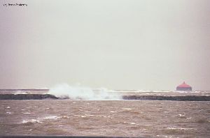 Waves crash over the breakwall by the intake crib light.